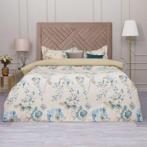 Può includere: Un letto con un set di piumino e cuscini a fantasia floreale. Il piumino presenta grandi fiori blu e beige su sfondo crema. La testiera è di colore marrone chiaro con un design geometrico.