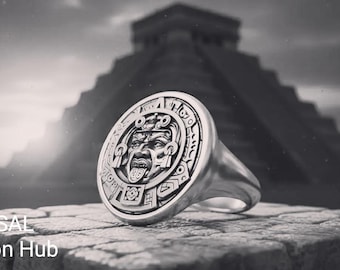 May include: A silver ring with a detailed Mayan-inspired design featuring a face with its tongue out. The ring is set against a backdrop of a pyramid, with the text "RASAL Fashion Hub" at the bottom.