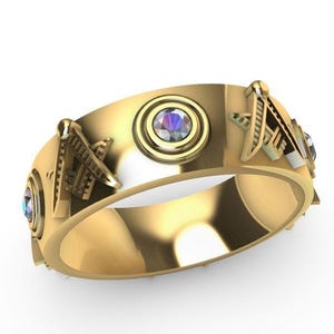 May include: A gold-colored ring with a unique design. The ring features a central iridescent stone surrounded by a circular setting, flanked by decorative elements. Additional iridescent stones are set on the ring's band. The text "RASAL Fashion Hub" is visible.