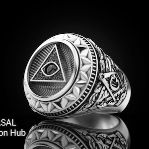 May include: A silver ring with a detailed design. The ring features a triangle with an eye in the center, surrounded by intricate patterns. The text "RASAL Fashion Hub" is visible at the bottom.