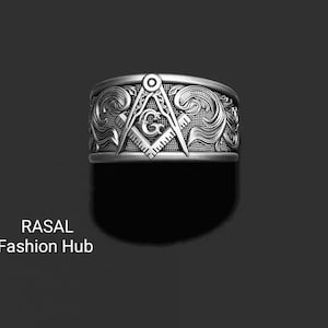 May include: A silver-colored ring with a Masonic symbol, featuring a compass and square design. The ring has an ornate, swirling pattern around the band. The text "RASAL Fashion Hub" is visible in the lower left corner.