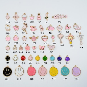 May include: A collection of gold-toned charms with colorful enamel details. The charms include various shapes such as hearts, flowers, butterflies, and smiley faces. Some charms feature a bunny, a flamingo, and a key. The charms are numbered from 182 to 229.