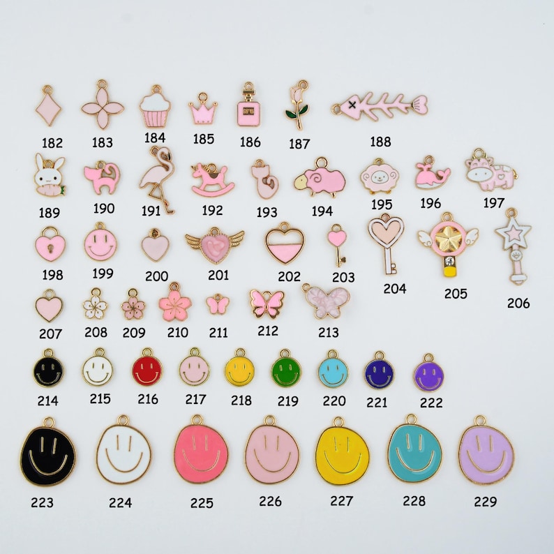 May include: A collection of gold-toned charms with colorful enamel details. The charms include various shapes such as hearts, flowers, butterflies, and smiley faces. Some charms feature a bunny, a flamingo, and a key. The charms are numbered from 182 to 229.