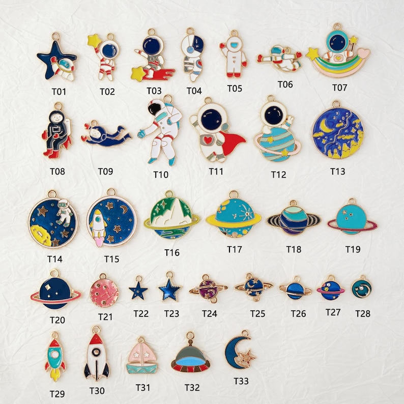 May include: A collection of colorful enamel charms with space-themed designs. The charms include astronauts, planets, rockets, stars, and moons. Each charm has a gold-colored loop for attaching to jewelry or other crafts.
