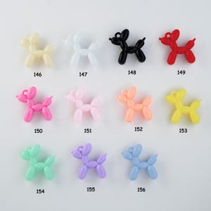 May include: A collection of colorful balloon dog charms in various colors, including yellow, white, black, red, pink, peach, light green, purple, and blue. Each charm has a loop for attaching to jewelry or other crafts. Numbers 146-156 are printed below each charm.