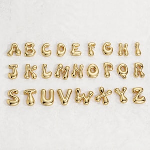 May include: A full alphabet of gold-colored, bubble-style letters arranged on a white surface. Each letter is individually crafted with a rounded, glossy finish. The letters are evenly spaced, creating a visually appealing display.