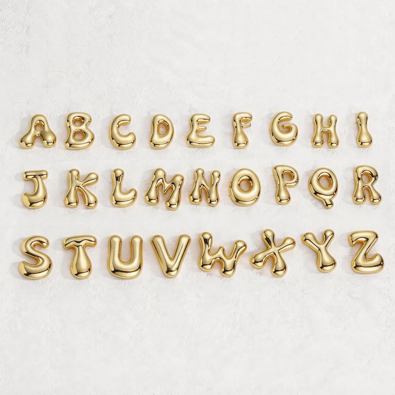 May include: A full alphabet of gold-colored, bubble-style letters arranged on a white surface. Each letter is individually crafted with a rounded, glossy finish. The letters are evenly spaced, creating a visually appealing display.