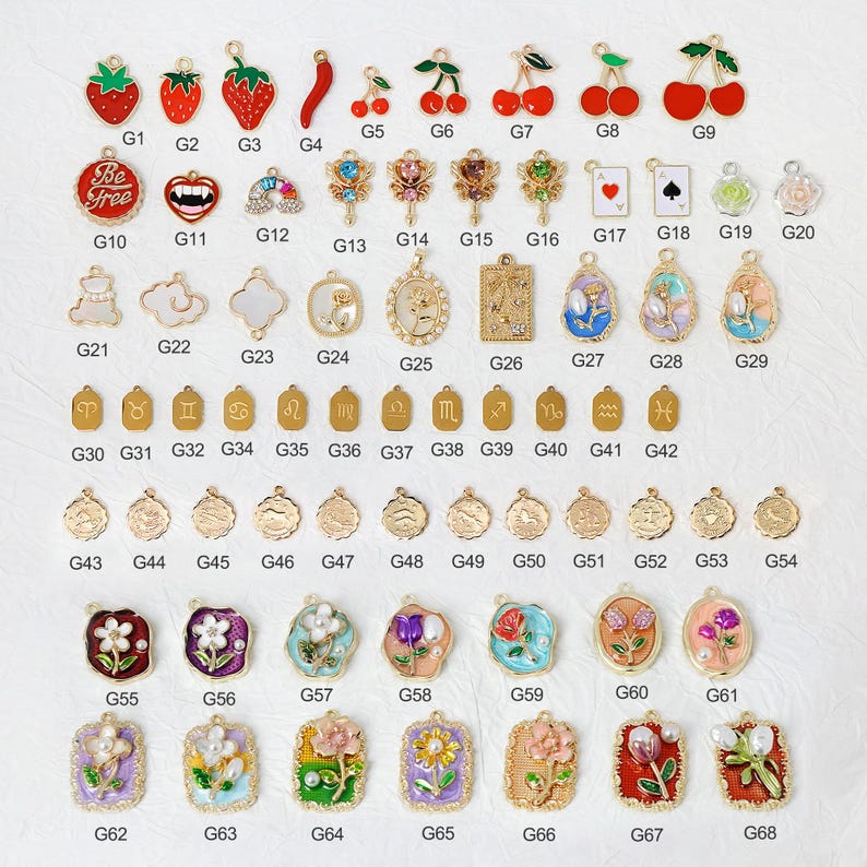 May include: A collection of gold-toned charms and pendants with various designs, including fruits, playing card suits, flowers, and zodiac symbols. Some charms feature enamel detailing in red, green, and blue. The charms are suitable for jewelry making.