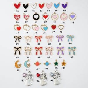 May include: A collection of metal charms in various shapes and colors, including hearts, bows, planets, stars, moons, and angels. Each charm has a loop for attaching to jewelry or crafts. Numbers are printed on each charm.