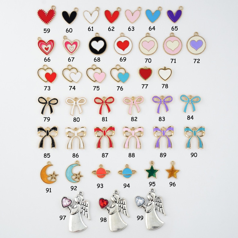 May include: A collection of metal charms in various shapes and colors, including hearts, bows, planets, stars, moons, and angels. Each charm has a loop for attaching to jewelry or crafts. Numbers are printed on each charm.