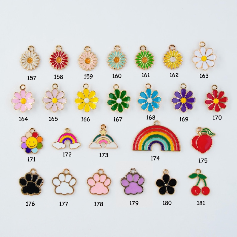 May include: A collection of colorful enamel charms in various shapes, including flowers, rainbows, paw prints, and a cherry. Each charm has a gold-colored border and a small loop for attaching to jewelry or other crafts. The charms are numbered 157-181.