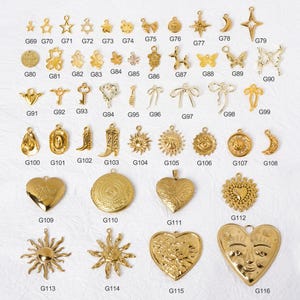 May include: A collection of gold-colored charms in various shapes, including stars, hearts, bows, and suns. The charms are arranged on a white surface, with each charm labeled with a number.