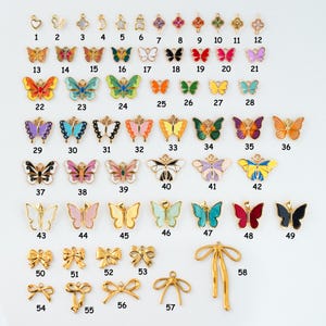 May include: A collection of gold-toned and colorful butterfly and bow charms. The charms are numbered 1-58 and vary in size, shape, and color. Some charms have enamel details, while others are plain gold.