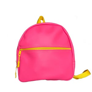 Puede incluir: Una mochila rosa brillante con cremallera, tirador y correas amarillas. La pequeña mochila tiene una parte superior redondeada y un bolsillo frontal con cremallera. Las correas de los hombros son amarillas.