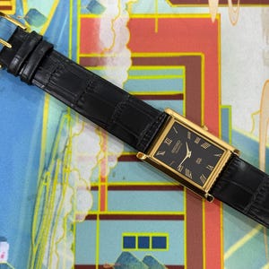May include: A rectangular gold-toned wristwatch with a black face and Roman numeral hour markers. The watch has a black leather band with a buckle closure. The watch face reads "SEIKO QUARTZ".