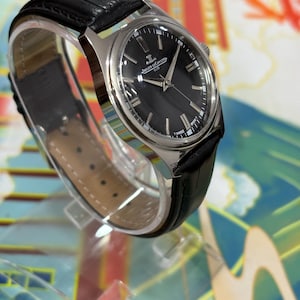 The black dial enhances readability while adding a bold and sophisticated touch, perfect for those who appreciate minimalist luxury watches. This close-up emphasizes the originality and condition of the dial, an important factor for vintage watch buyers seeking authenticity and quality. Ideal for collectors of Swiss watches, retro watches, and luxury dress watches, this Jaeger-LeCoultre Club model is a rare find.