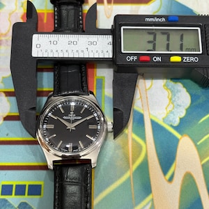 Close-up view of an authentic vintage Jaeger-LeCoultre Club watch dial, highlighting the elegant black dial design and fine detailing of this classic Swiss timepiece. The dial features clean hour markers, slim hands, and a timeless layout that reflects the refined craftsmanship of Jaeger-LeCoultre. This manual wind mechanical watch showcases precision engineering and vintage charm, making it highly desirable among collectors and watch enthusiasts.