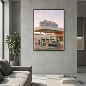 May include: A framed print depicting a vintage gas station, "Sunset Gas", in pastel shades. The gas station features a pink and teal colour scheme, with a classic car parked nearby. The word "Coffee" is visible on the building.
