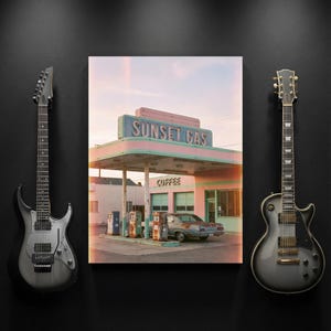 May include: A framed print of a vintage gas station with the text "Sunset Gas" in pink and blue. Two electric guitars flank the print on a black background. The gas station has a retro aesthetic.