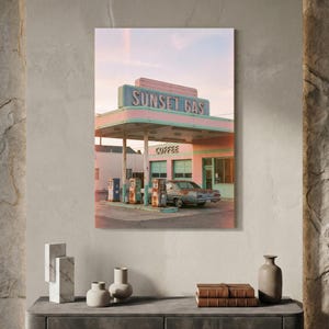 May include: A photograph of a retro gas station with the text "SUNSET GAS" in blue neon. The gas station is painted in pastel pink and green, with a classic car parked underneath the canopy. The word "COFFEE" is also visible.