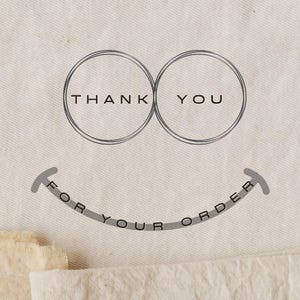 May include: A light beige fabric with a grey graphic. The graphic includes two overlapping circles with the words "THANK YOU" inside. Below, a curved line reads "FOR YOUR ORDER".