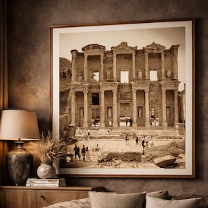 Puede incluir: Una impresión enmarcada en tonos sepia de una antigua estructura romana cuelga sobre un sofá de cuero marrón. La habitación cuenta con un mueble de madera, una mesa con una vela y una lámpara. La estética general es cálida y acogedora, con tonos neutros.