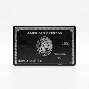Può includere: Una carta di credito American Express nera con scritte e dettagli argentati. La carta presenta il logo American Express, un profilo di un centurione romano e il nome del titolare della carta, John M Garrity II.
