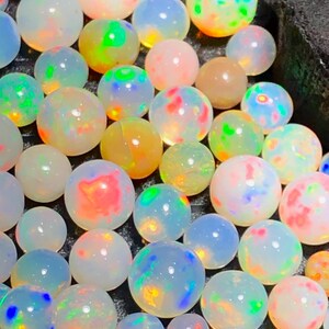 May include: A collection of round, translucent opals featuring a play-of-color effect with flashes of neon green, bright orange, and electric blue. These smooth, polished gemstones are arranged closely together, displaying internal fire and iridescence.