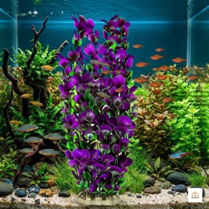 Op de afbeelding: Een hoge, kunstmatige aquariumplant met levendige paarse bladeren met groene accenten aan de basis, rechtopstaand in een aquarium gevuld met water, donker drijfhout, groene waterplanten en verschillende kleine oranje vissen die rondzwemmen.