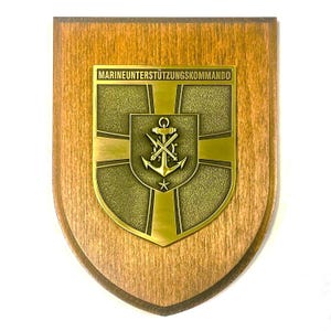 Op de afbeelding: Houten schild met een goudkleurig embleem. Het embleem toont een anker, gekruiste gereedschappen en een ster, met de tekst "MARINEUNTERSTÜTZUNGSKOMMANDO". Het schild heeft een schildvorm.