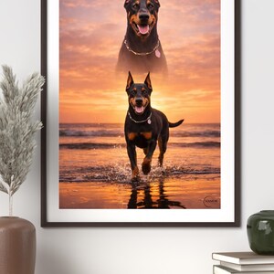 K&ouml;nnte beinhalten: Gerahmter Druck mit zwei Dobermann Pinschern vor einem Sonnenuntergang. Ein Hund rennt durch Wasser. Beide Hunde tragen Halsb&auml;nder. Der Himmel ist eine Mischung aus Orange und Gelb.