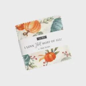May include: A bundle of fabric squares with a fall-themed design, showcasing pumpkins, leaves, and berries in orange, green, and cream hues. The fabric is wrapped with a label that reads "I LOVE Fall MOST OF ALL!" by Deb Strain.