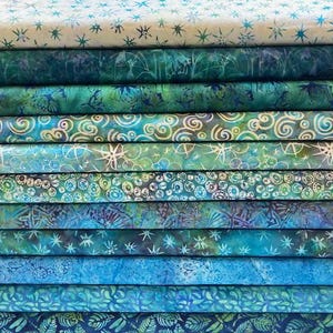 Peut inclure: Une pile de douze rouleaux de tissu pliés présentant divers motifs batik dans des tons de bleu, sarcelle, vert et crème. Les designs incluent des étoiles, des lignes tourbillonnantes, des cercles, des fleurs et des libellules sur coton.