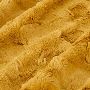 May include: Close-up of a soft, plush fabric in a warm mustard yellow colour. The fabric has a fuzzy texture and a slightly rippled pattern.