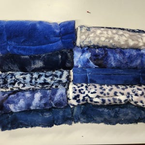 May include: A stack of blue and white faux fur fabric scraps. The fabric has a variety of patterns, including solid blue, blue and white swirls, and a leopard print.