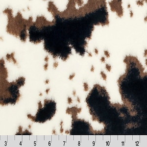 May include: White fabric with brown and black cowhide print. The fabric has a soft, fuzzy texture.