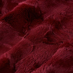 Könnte beinhalten: Nahaufnahme eines plüschigen, burgunderfarbenen Kunstpelzes. Der Stoff hat eine weiche, samtige Textur und eine tiefe, satte Farbe.