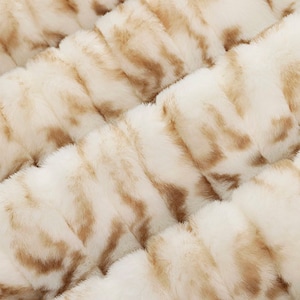 Pu&ograve; includere: Primo piano di un tessuto in pelliccia sintetica bianco e marrone con una texture morbida e soffice.