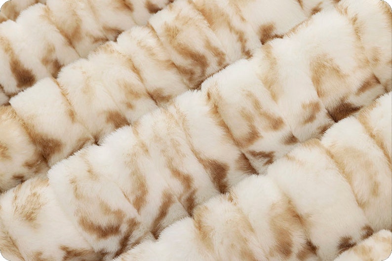 Pu&ograve; includere: Primo piano di un tessuto in pelliccia sintetica bianco e marrone con una texture morbida e soffice.