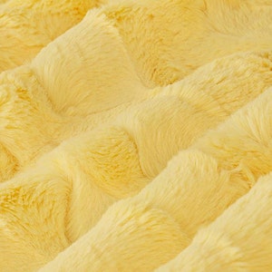 May include: A close-up of a soft, yellow faux fur fabric with a textured, quilted pattern.
