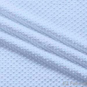 Könnte beinhalten: Nahaufnahme eines hellblauen Stoffes mit einem erhabenen Punktmuster. Der Stoff ist gefaltet, wodurch Schatten entstehen und die Textur hervorgehoben wird. Das Material wirkt weich und könnte für verschiedene Nähprojekte verwendet werden.