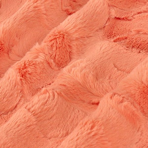 May include: Close-up of a soft, peach-coloured faux fur fabric. The fabric has a plush, velvety texture and a subtle sheen.