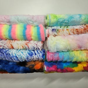 May include: A stack of colorful fluffy fabric rolls in various tie-dye patterns, including rainbow stripes, ombre, and swirls.