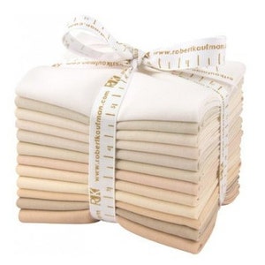 Può includere: Un pacco di 12 quarti di tessuto in varie tonalità di beige e crema, legati insieme da un nastro bianco con testo dorato che recita "www.robertkaufman.com".