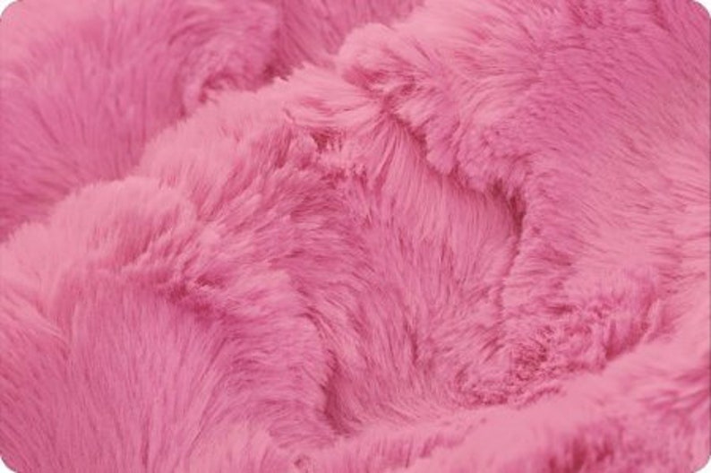 May include: Close-up of a soft, pink faux fur fabric. The fabric has a fluffy texture and a subtle sheen.
