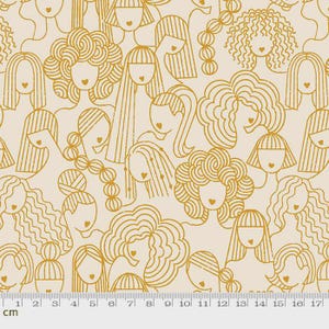Puede incluir: Tela crema con un patrón repetido de rostros femeninos estilizados en dorado. Los rostros tienen varios peinados y detalles en forma de corazón. Una regla en centímetros es visible en la parte inferior.