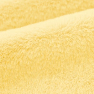 May include: Close-up of a soft, yellow faux fur fabric. The fabric has a fluffy texture and a subtle sheen.