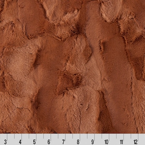 May include: Close-up of a brown faux fur fabric with a textured, wavy pattern. The fabric has a soft, plush feel.