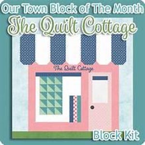 May include: A quilt block pattern titled Our Town Block of The Month The Quilt Cottage. The design features a pink storefront with a blue and white striped awning, a green geometric window display, and a door with the text The Quilt Cottage.