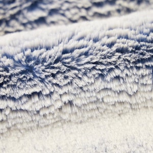 May include: Close-up of a soft, blue and white faux fur fabric. The fabric has a fluffy texture and a subtle ombre effect.
